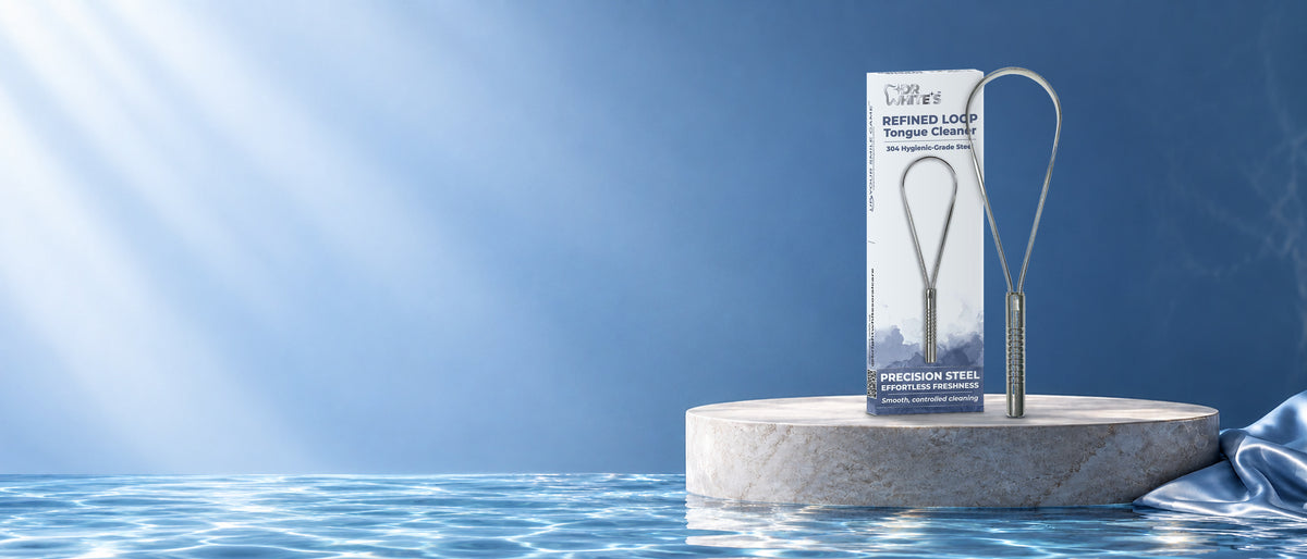 Dr. White’s Refined Loop stainless steel tongue cleaner and original carton on a cool stone pedestal beside blue water.